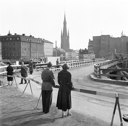 Några personer står och ser ut över bron. Klara kyrka i bakgrunden.