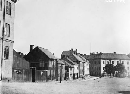 En gatuvy, med en lång rad av hus av olika höjd. gammal träbebyggelse och stenhus.