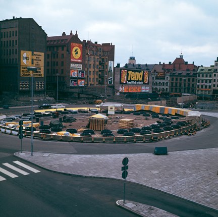 Byggnader med stora reklamskyltar på fasaderna, tillfälliga plank och avspärrningar under byggnationer vid Sergels torg