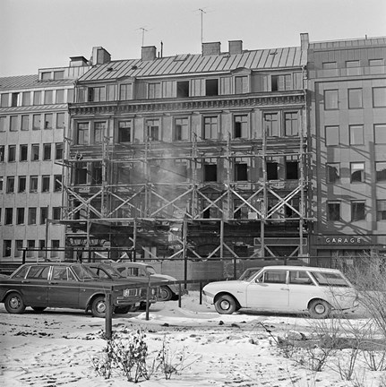 Byggnadsställning framför fasaden. Vy från andra sidan gatan, vid parkeringsplats.