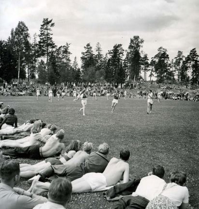 Ungdomar ligger i gräset, tittar på andra som springer på en fotbollsplan.