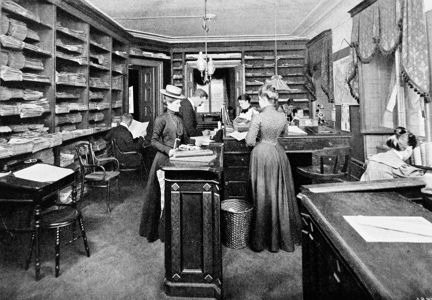 interiör av ett kontor med hyllor längs väggarna, fulla med papper och tdningar. en kvinna står bakom en disk och hjälper kunder, två kvinnor och en man. en av männen sitter i en stol och läser en tidning. kvinnorna är klädda i långa kjolar och hattar.